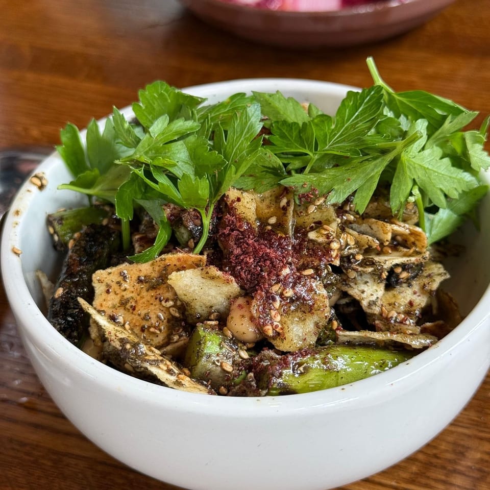 Close-up of a seasoned dish topped with fresh parsley and red spices in a white bowl on a wooden table.
