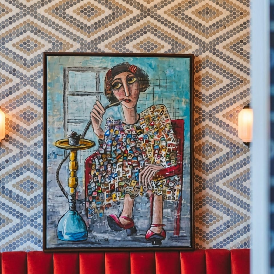 Framed painting of a woman smoking a hookah, displayed on geometric patterned walls above a red restaurant banquette.